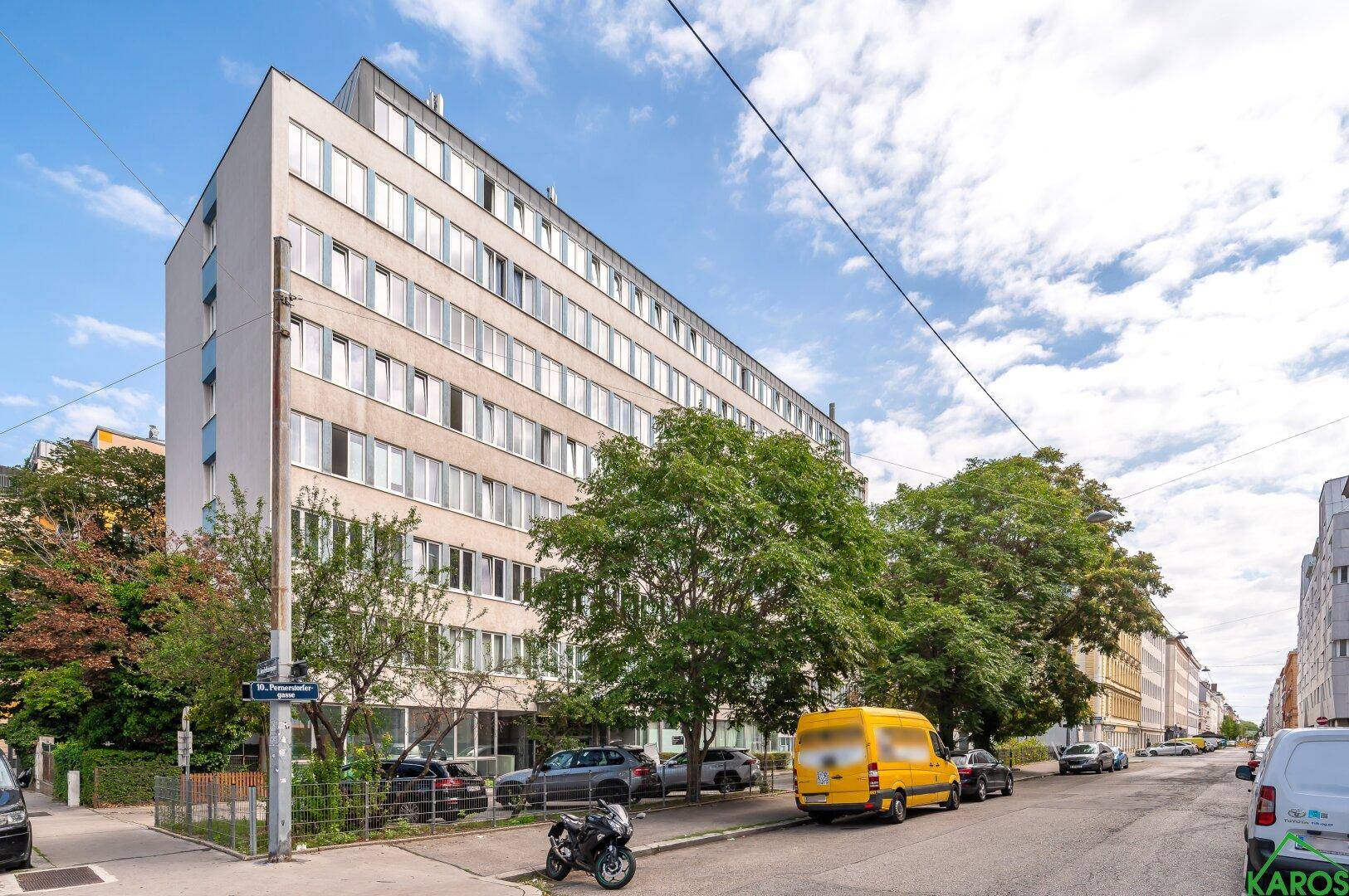 Ansicht des Wohngebäudes von der Straßenseite mit parkenden Autos und Bäumen.