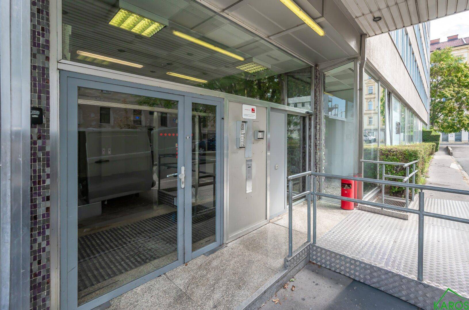 Eingangsbereich des Gebäudes mit Glastüren und einer barrierefreien Rampe für den Zugang.