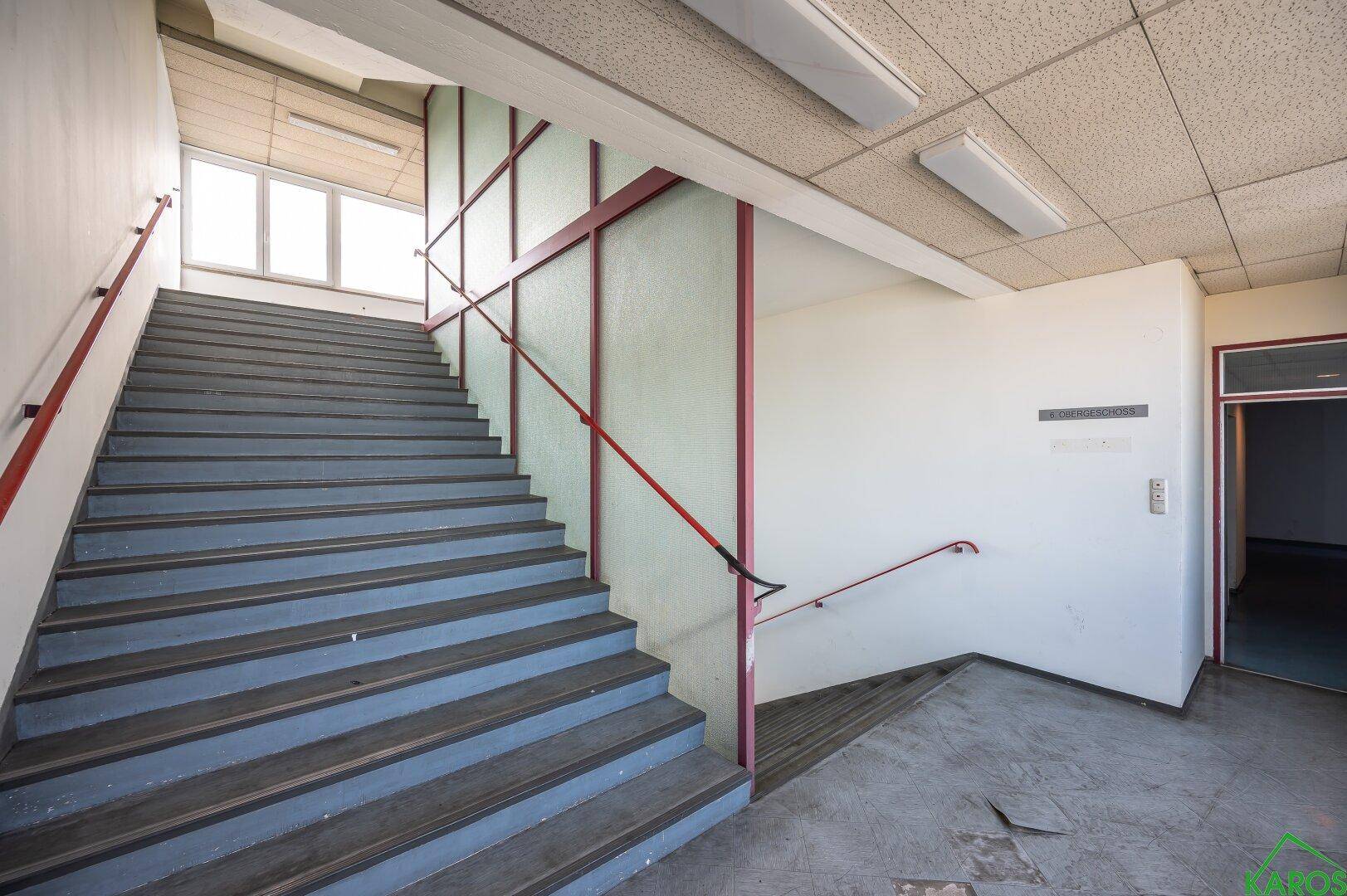 Treppenhaus mit breiten Stufen und roten Handläufen, das zu den oberen Etagen führt.