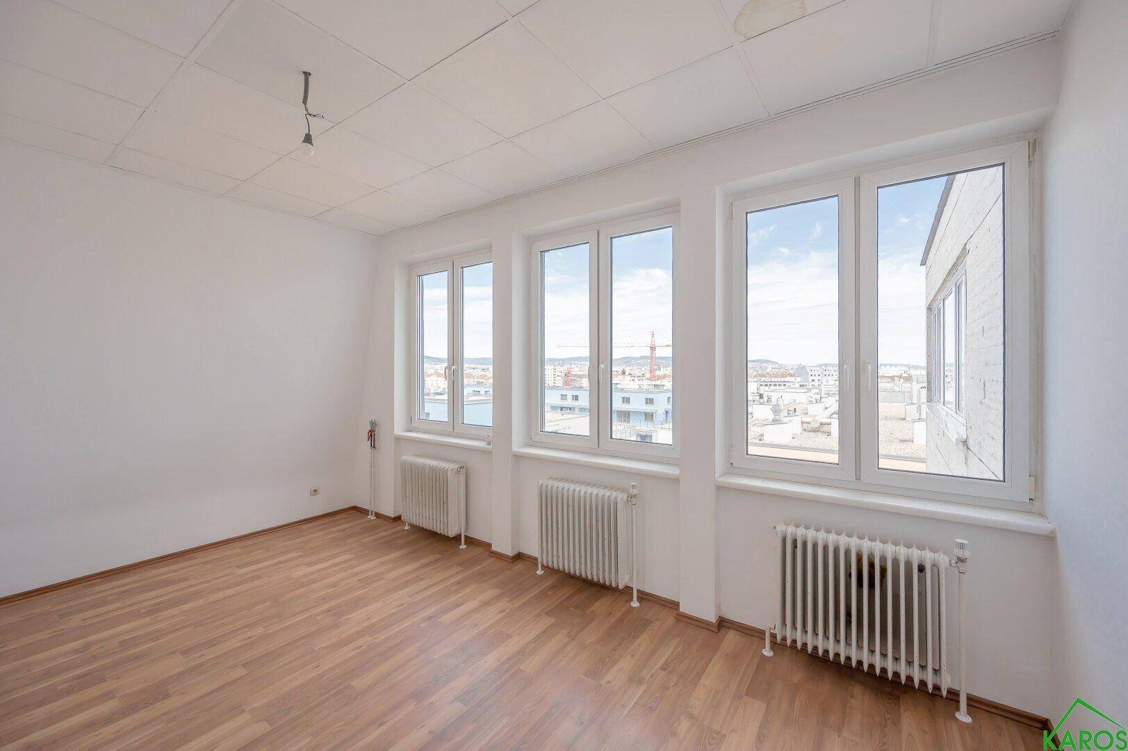 Helles Wohnzimmer mit Holzfußboden, großen Fenstern und Blick auf die Stadt.