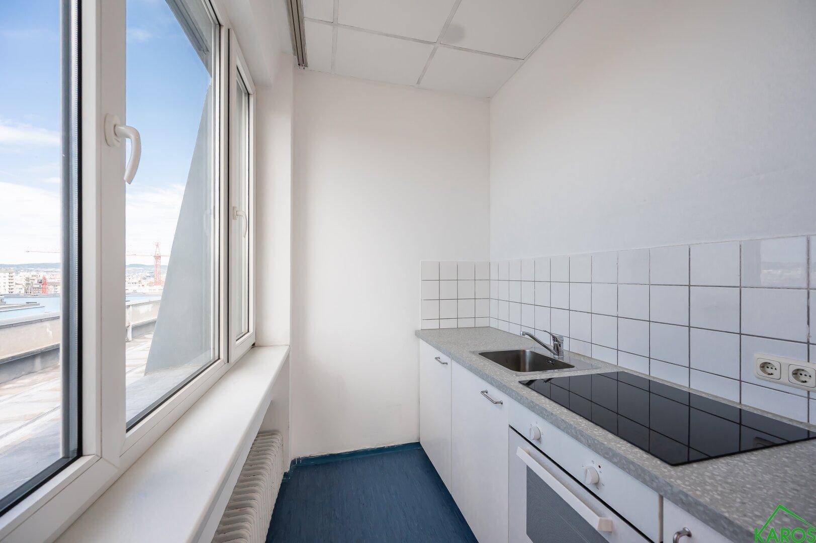 Kleine Küche mit weißen Schränken, Kochfeld, Backofen und großem Fenster mit Ausblick.