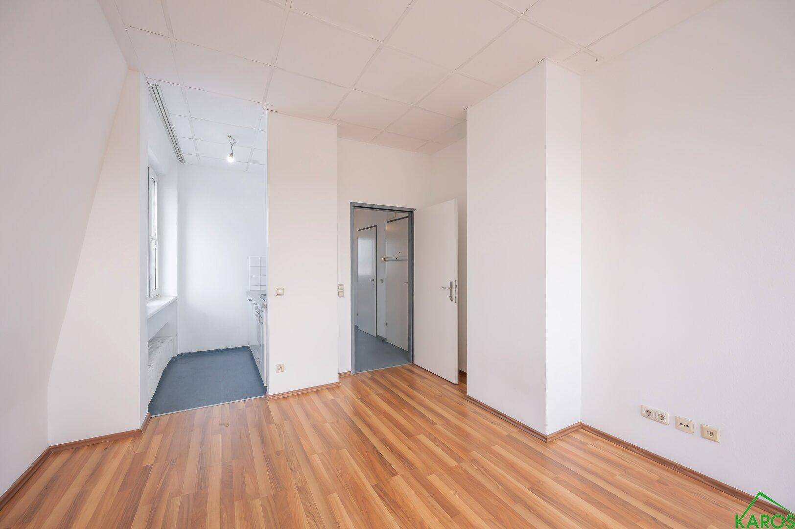 Heller Raum mit Holzfußboden, der zu einer kleinen Küche und einem weiteren Zimmer führt.