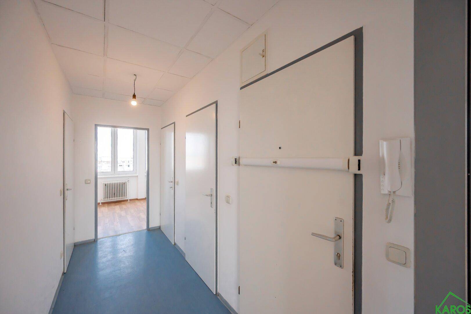 Langer Flur mit blauem Linoleumboden und Türen zu verschiedenen Zimmern der Wohnung.