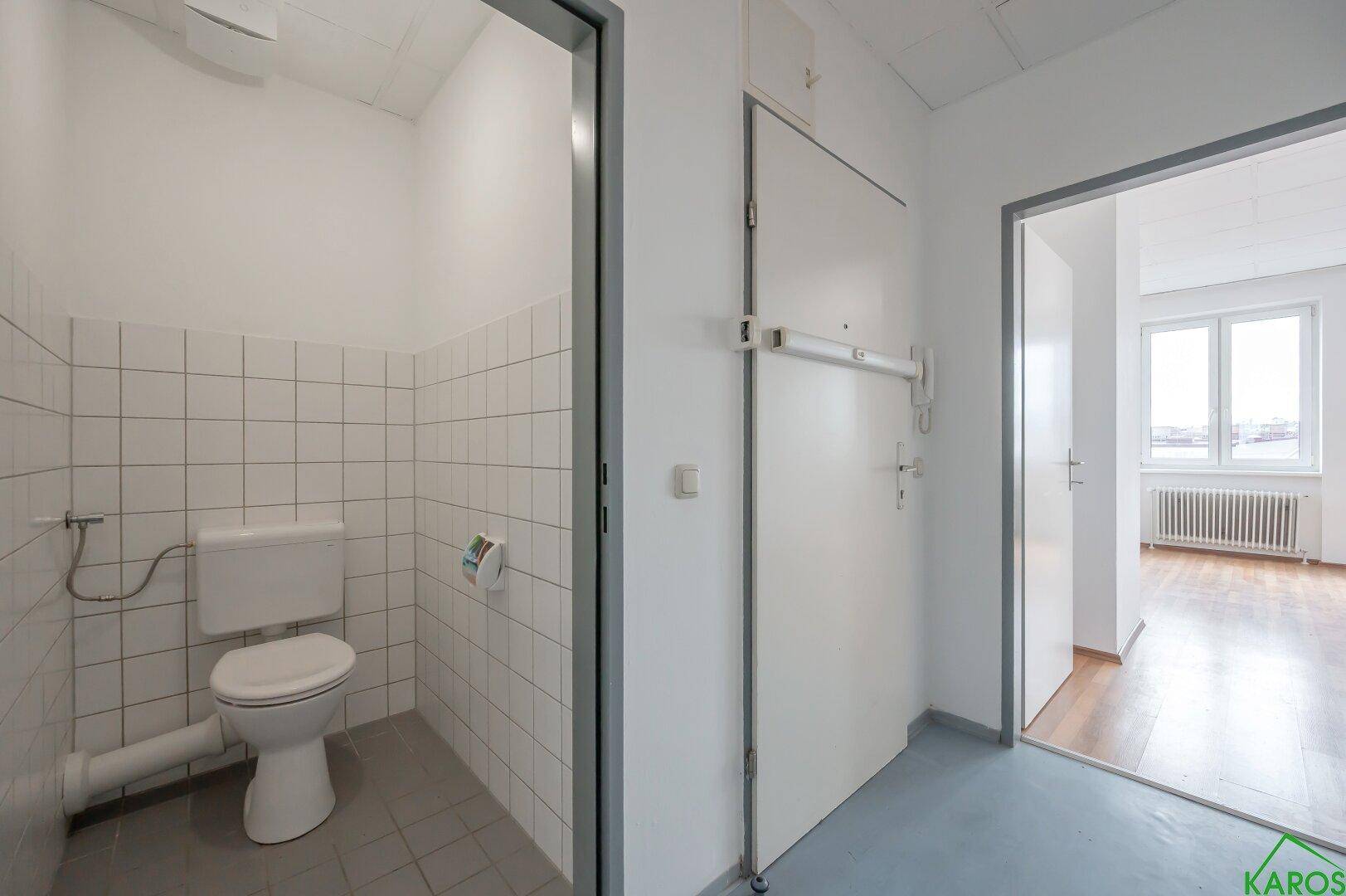 Flur mit Zugang zu einem separaten WC mit weißen Fliesen und Toilette.