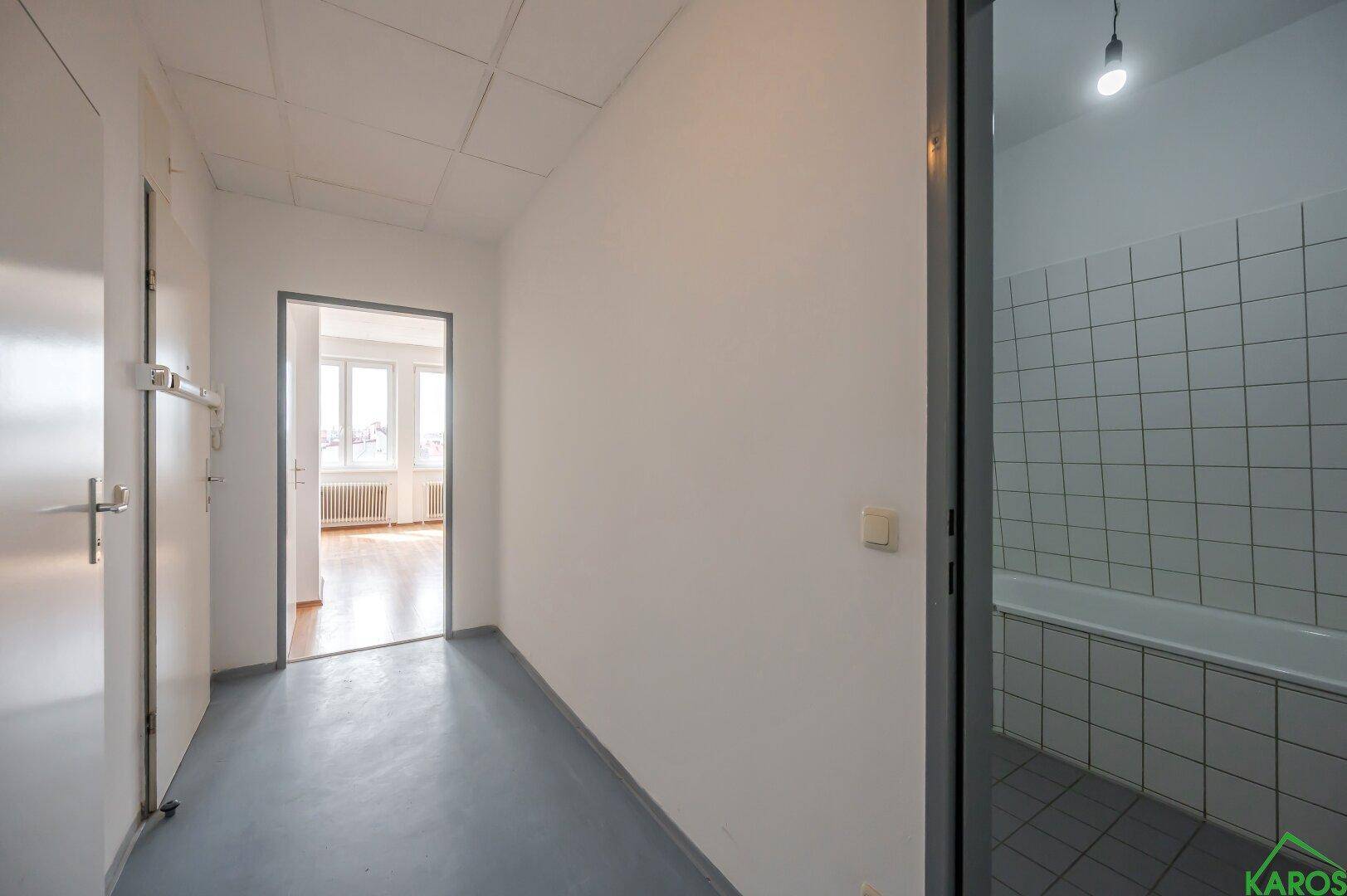 Flur mit blauem Bodenbelag und offener Tür zu einem Badezimmer mit Badewanne.