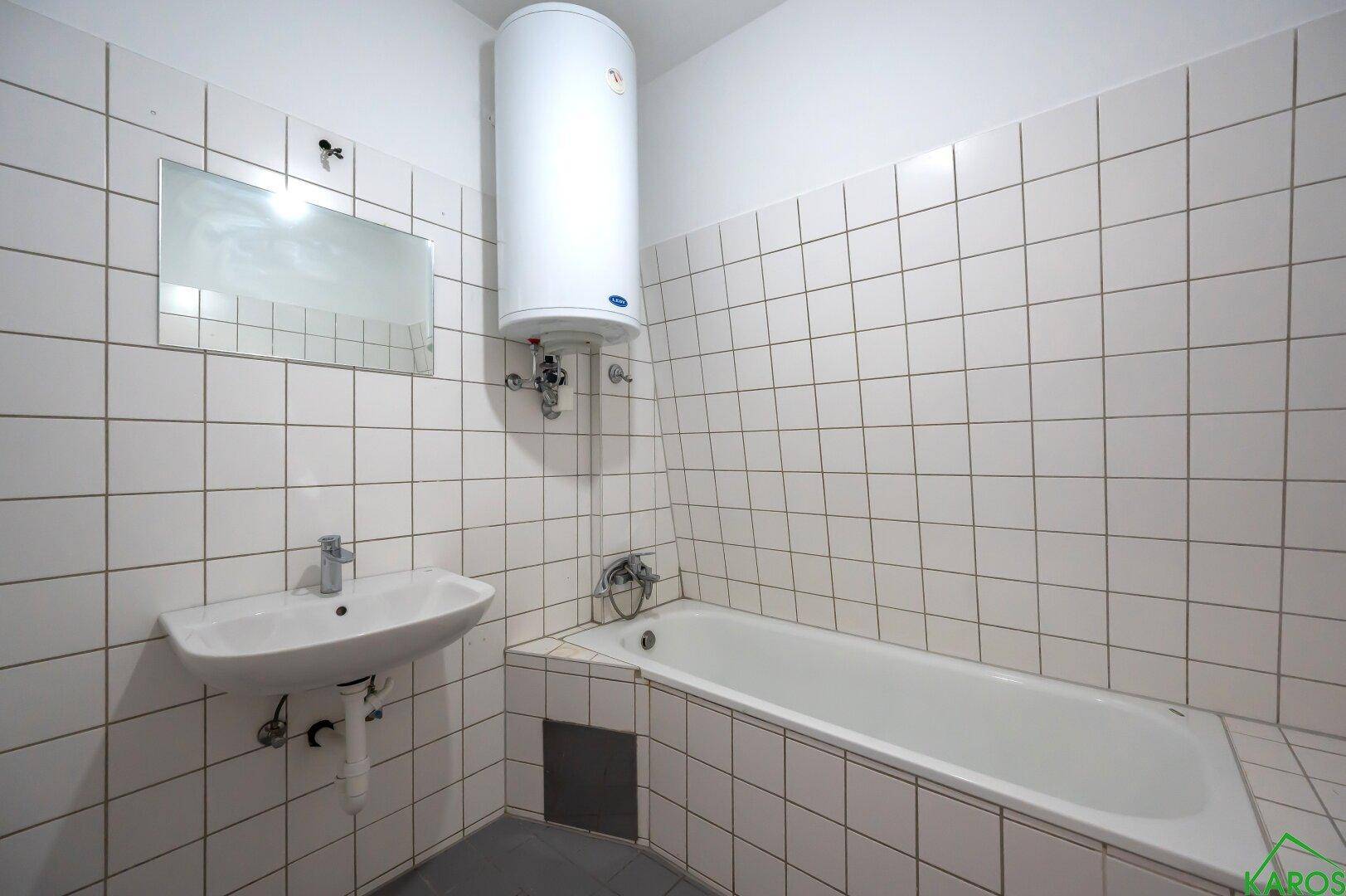Einfaches Badezimmer mit Badewanne, Waschbecken, Boiler und weißen Wandfliesen.