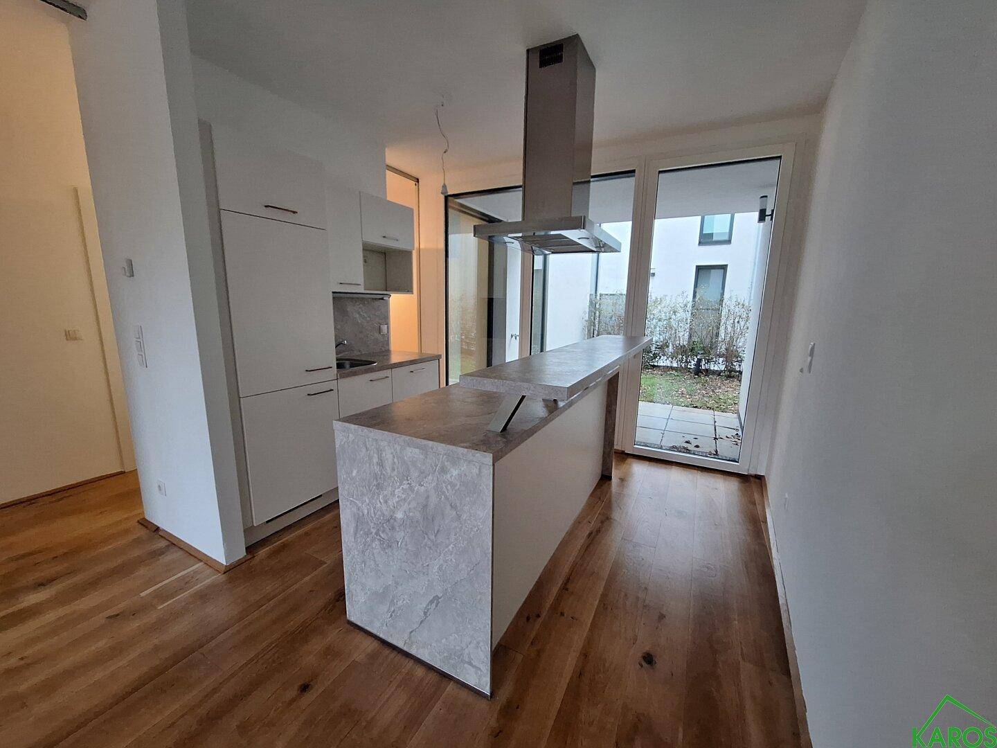 Helle, moderne Küche mit Kochinsel, Dunstabzugshaube und Zugang zum Gartenbereich.