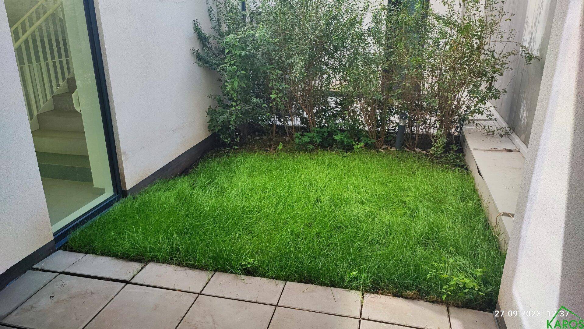 Kleiner, gepflegter Gartenbereich mit Rasenfläche und Steinplatten, ideal zum Entspannen.