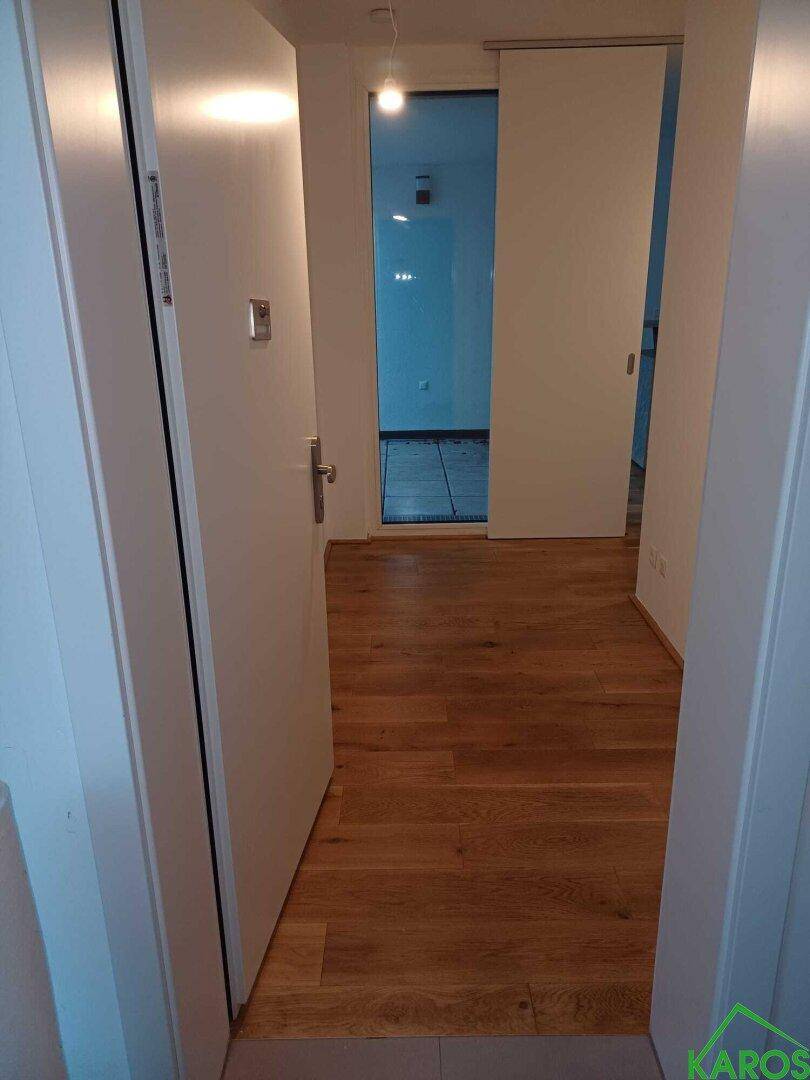 Heller Flur mit Holzboden und weißen Türen, der zu weiteren Räumen führt.