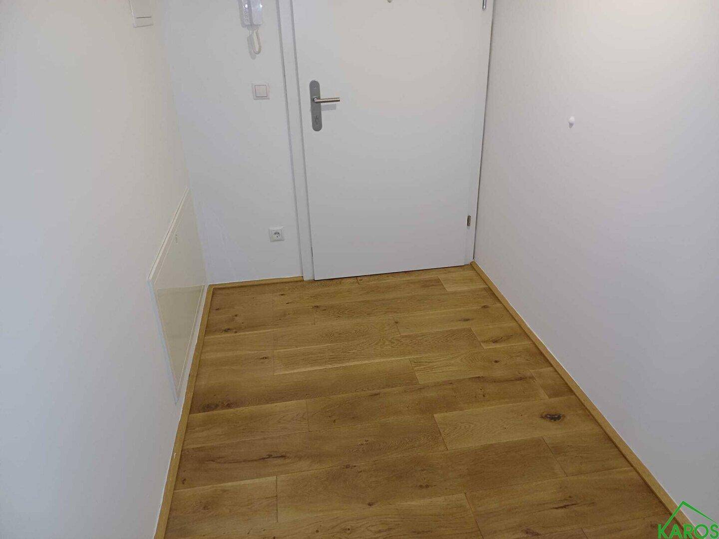 Eingangsbereich mit Holzboden und weißer Tür, der einen sauberen und modernen Eindruck vermittelt.