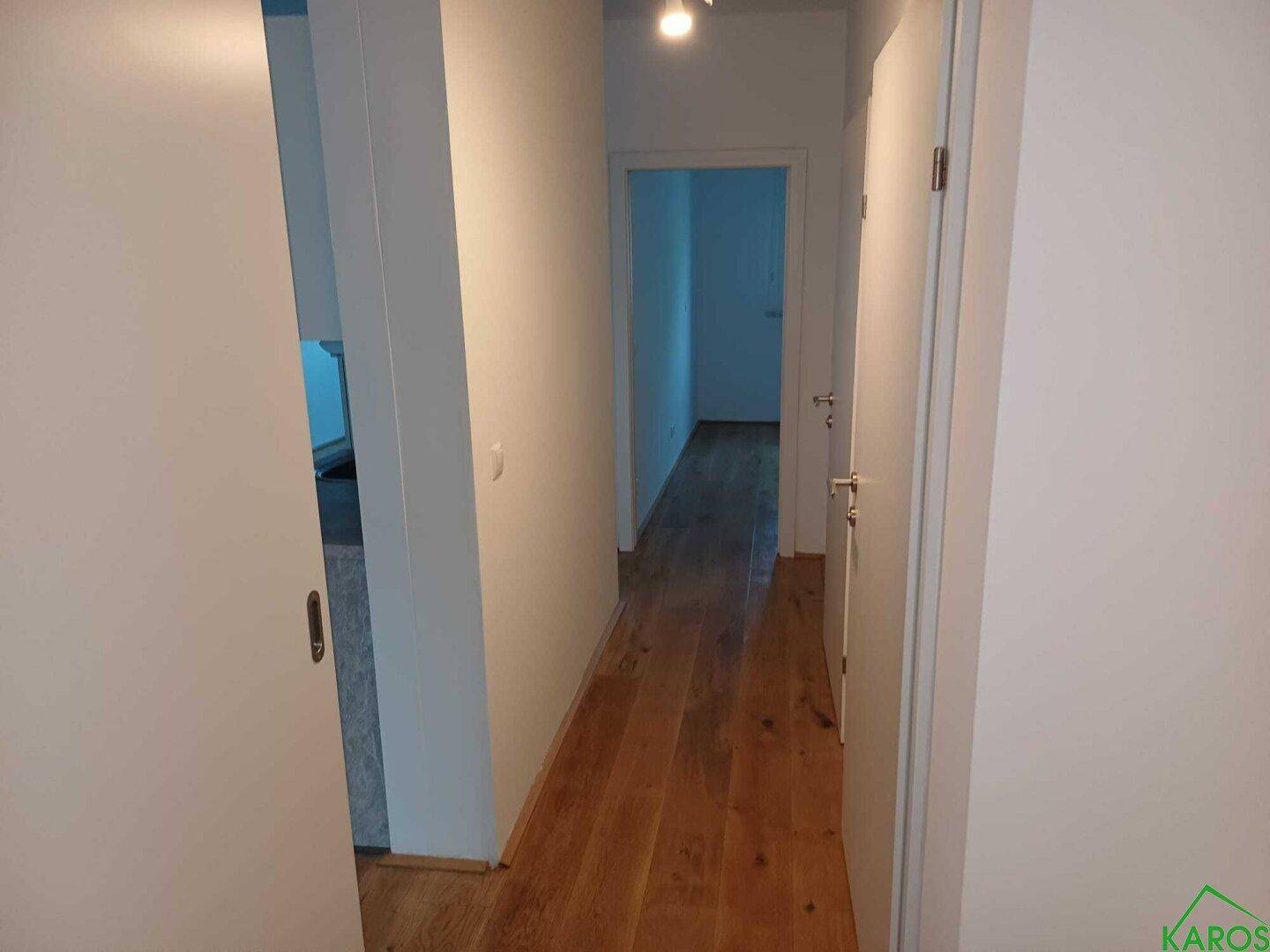 Langer, heller Flur mit Holzboden und weißen Wänden, der verschiedene Zimmer verbindet.