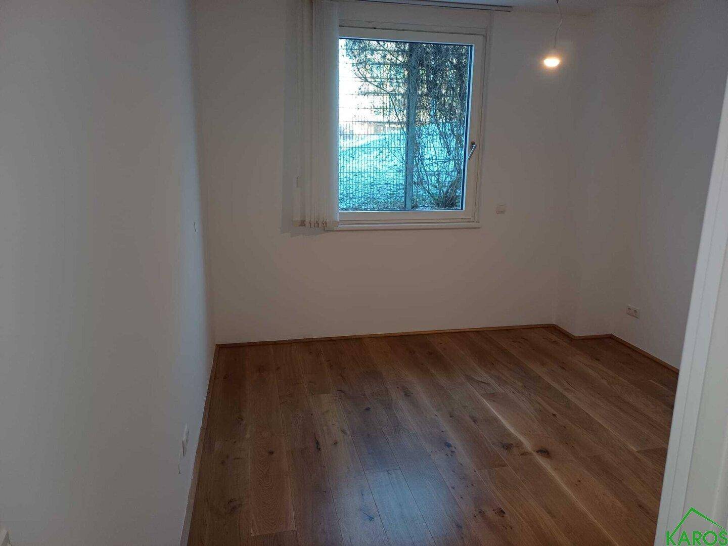 Helles Schlafzimmer mit Holzboden und einem Fenster, das den Blick nach draußen freigibt.