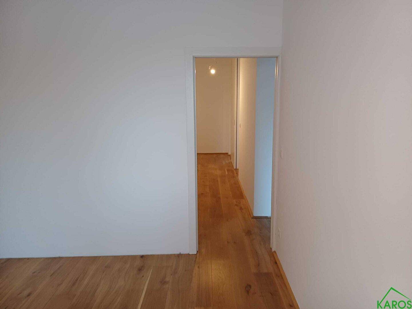 Heller Raum mit Holzboden und Zugang zu einem weiteren Flur oder Zimmer.