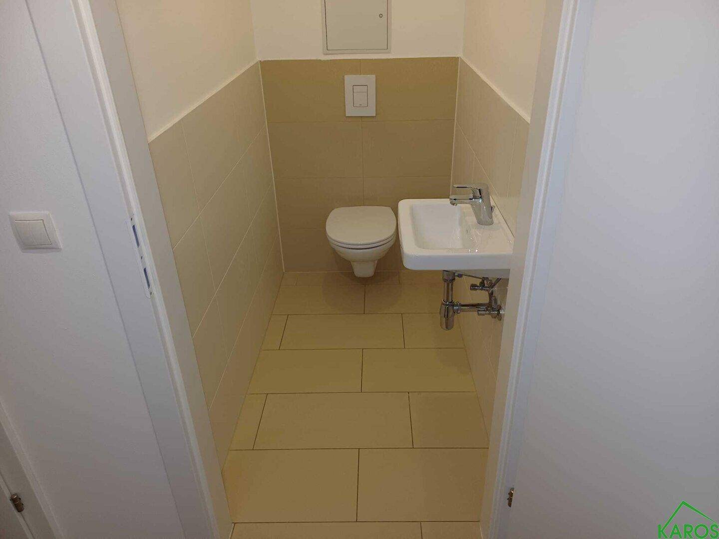 Kleines Gäste-WC mit Wand-WC und Handwaschbecken, hell gefliest.
