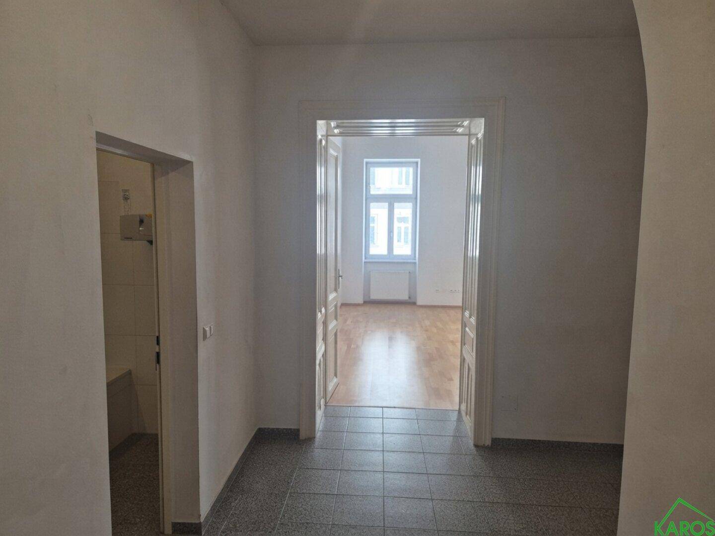 Heller Flur mit Fliesenboden, der zu einem Zimmer mit Parkettboden führt.
