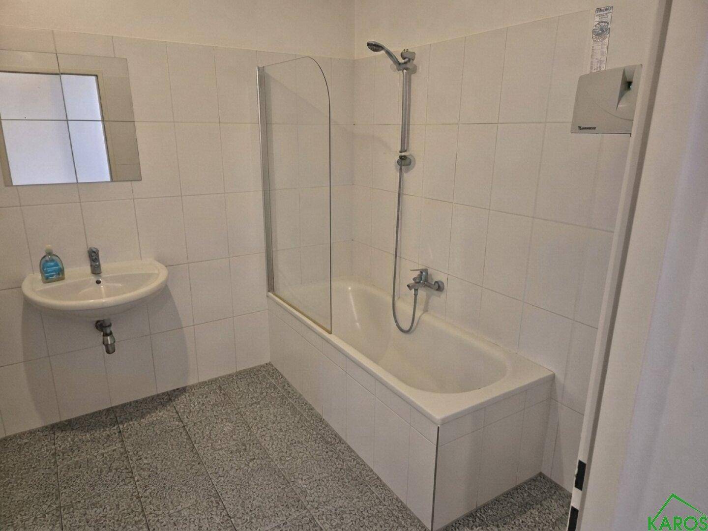 Badezimmer mit Badewanne, Duschvorrichtung, Waschbecken und weißen Fliesen an Wänden und Boden.