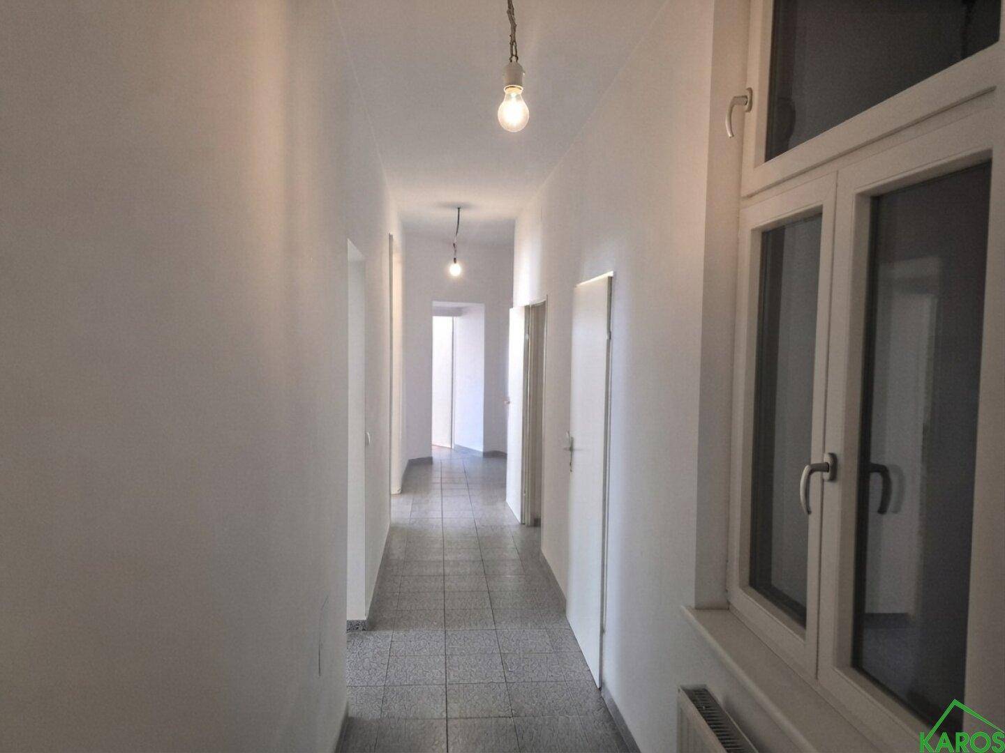 Langer, heller Flur mit Fliesenboden und einem Fenster, das Tageslicht hereinlässt.