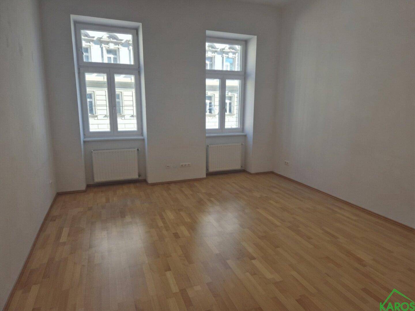 Geräumiges Zimmer mit hellem Parkettboden und zwei großen Fenstern für viel Tageslicht.