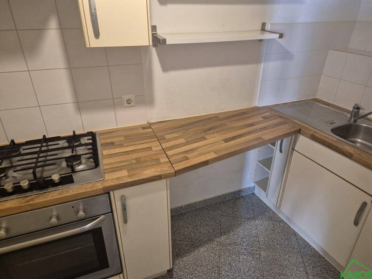 Küche mit Gasherd, Backofen, Spüle und Arbeitsplatte aus Holz, auf Fliesenboden.