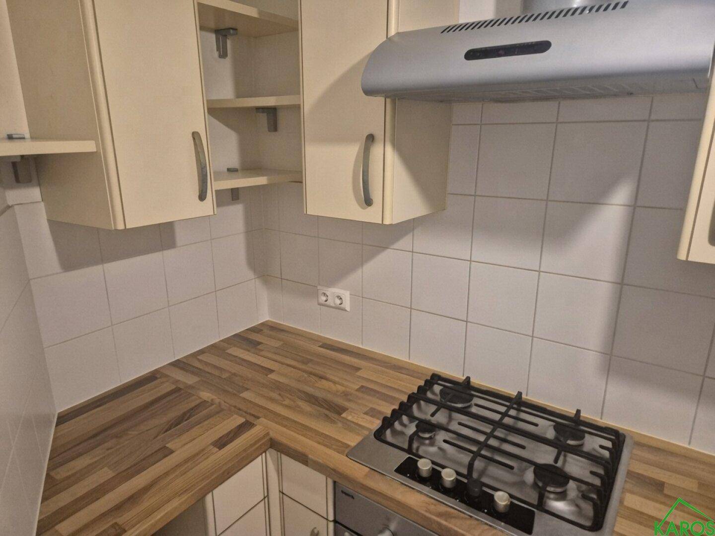 Küchenzeile mit Gasherd, Dunstabzugshaube und weißen Wandfliesen über der Arbeitsplatte.