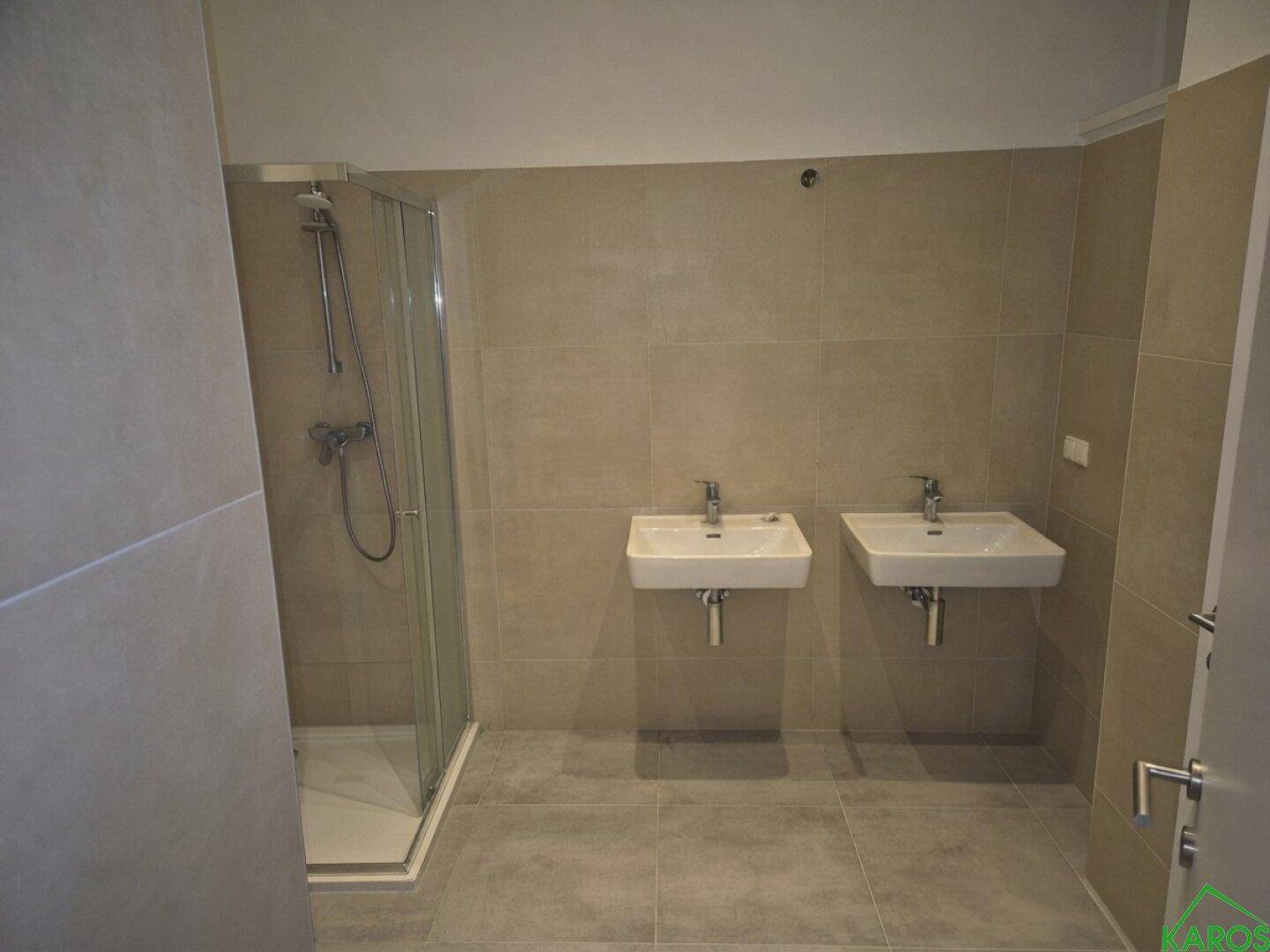 Geräumiges Badezimmer mit zwei Waschbecken, Duschkabine und großformatigen Fliesen.