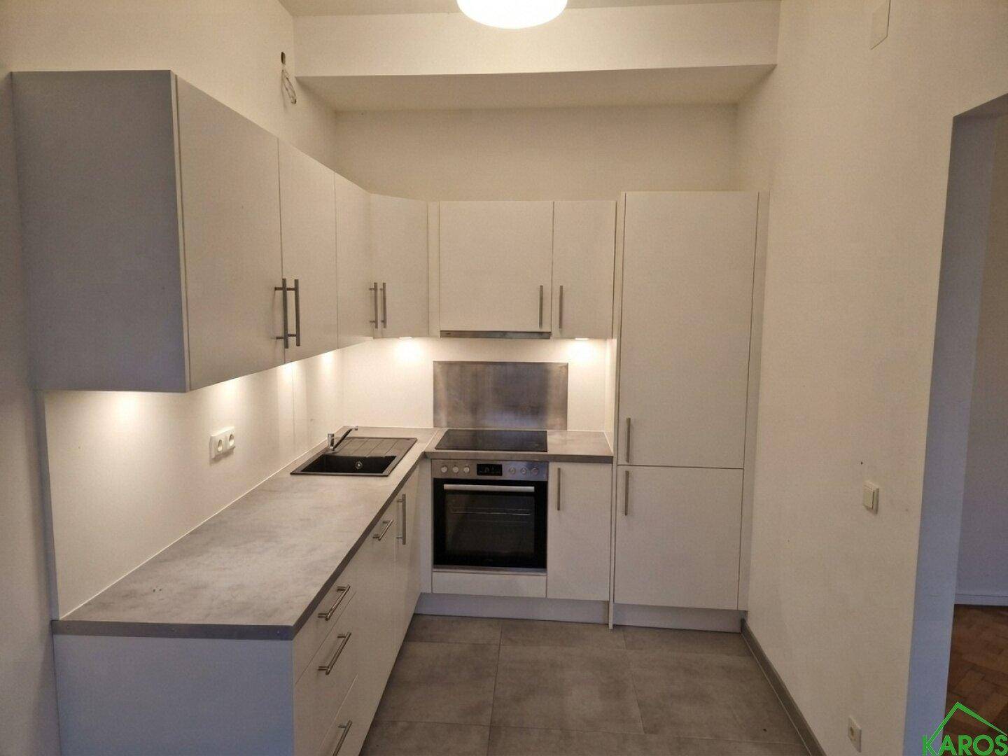 Moderne Einbauküche mit weißen Schränken, grauer Arbeitsplatte und integrierten Elektrogeräten.