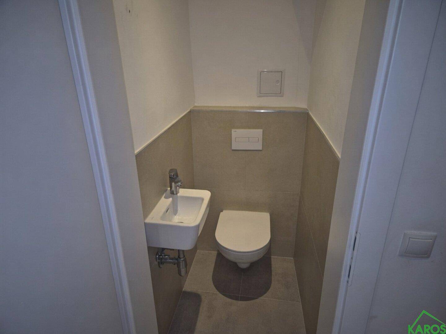Kleines Gäste-WC mit wandhängendem WC, Handwaschbecken und hellen Fliesen.