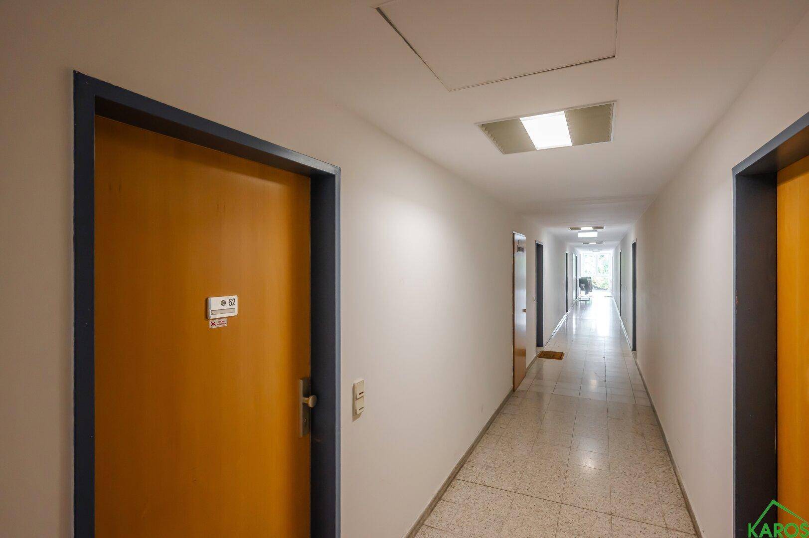 Langer, heller Gemeinschaftsflur mit mehreren Türen und Fliesenboden.