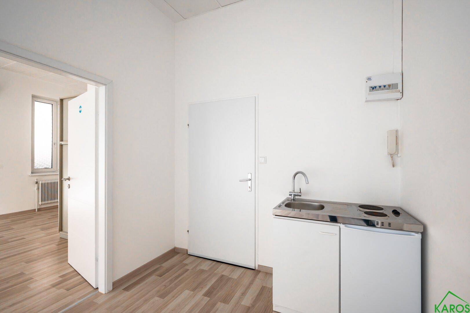 Detailansicht einer kleinen Küchenzeile mit Spüle, Kochfeld und Kühlschrank in einem Büroraum.