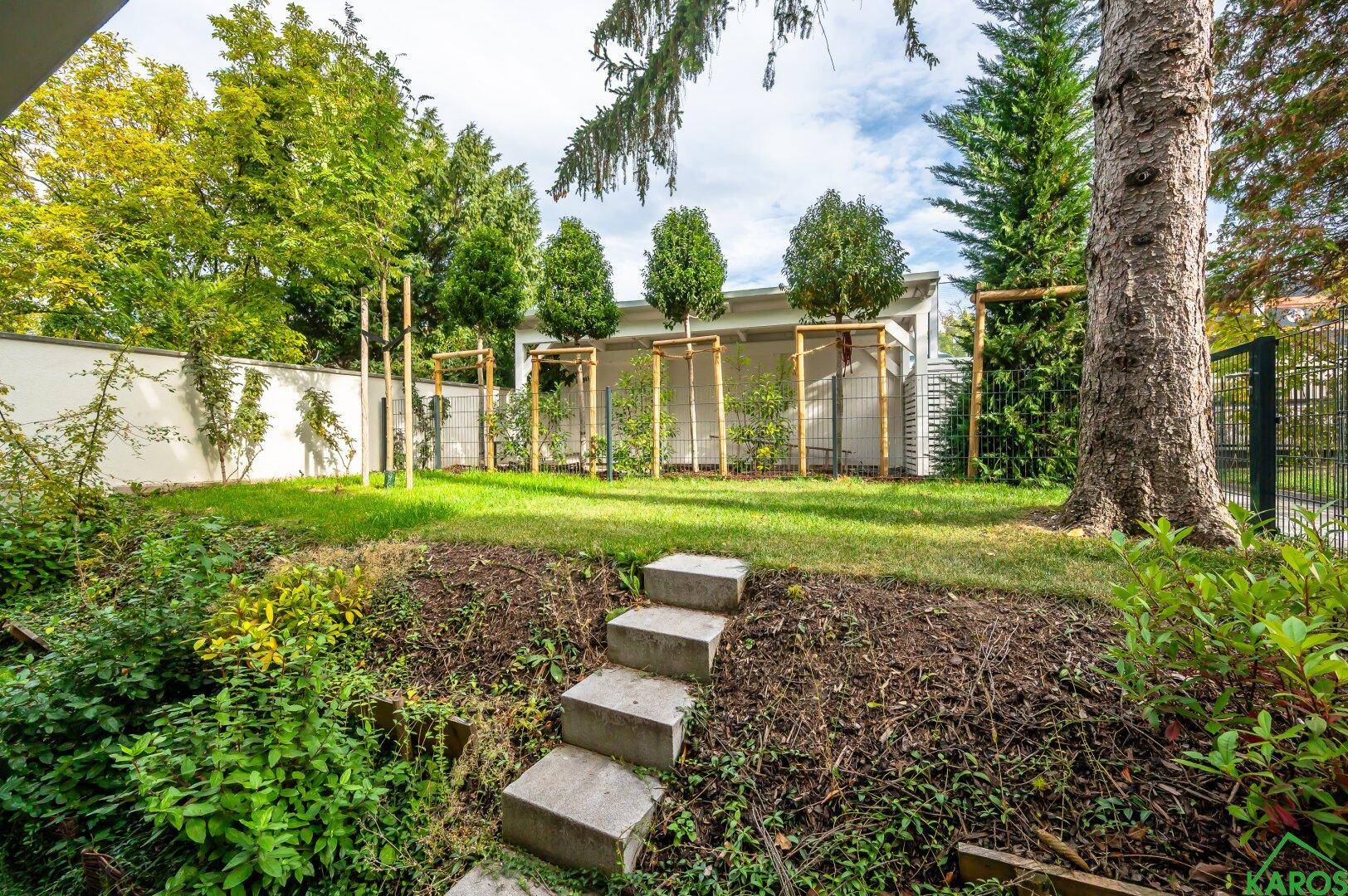 Grüner Gartenbereich mit Rasenfläche und Treppe, umgeben von Bäumen und Sträuchern.