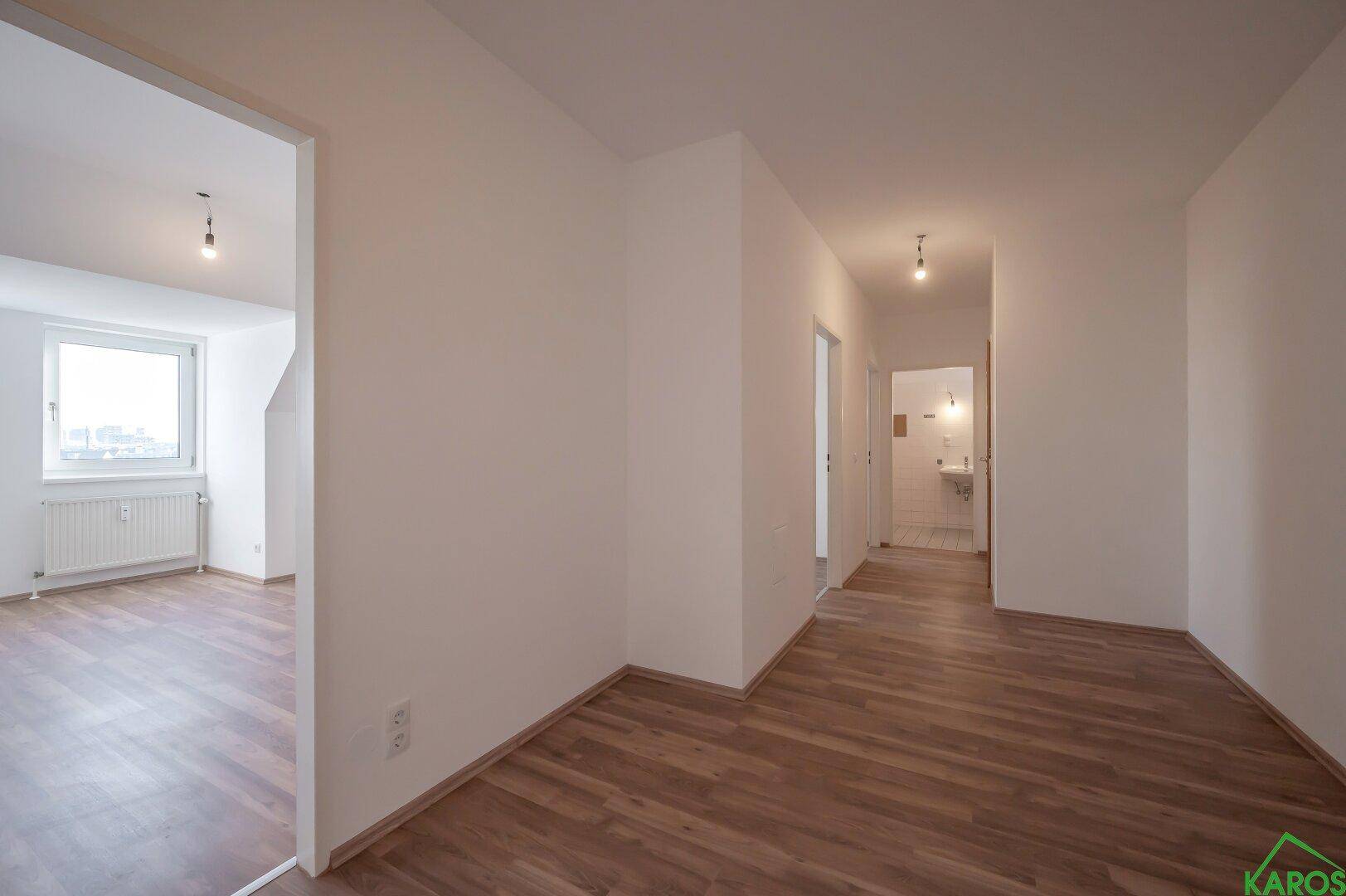 Langer Flur mit Laminatboden und Blick in ein Badezimmer mit Waschbecken.