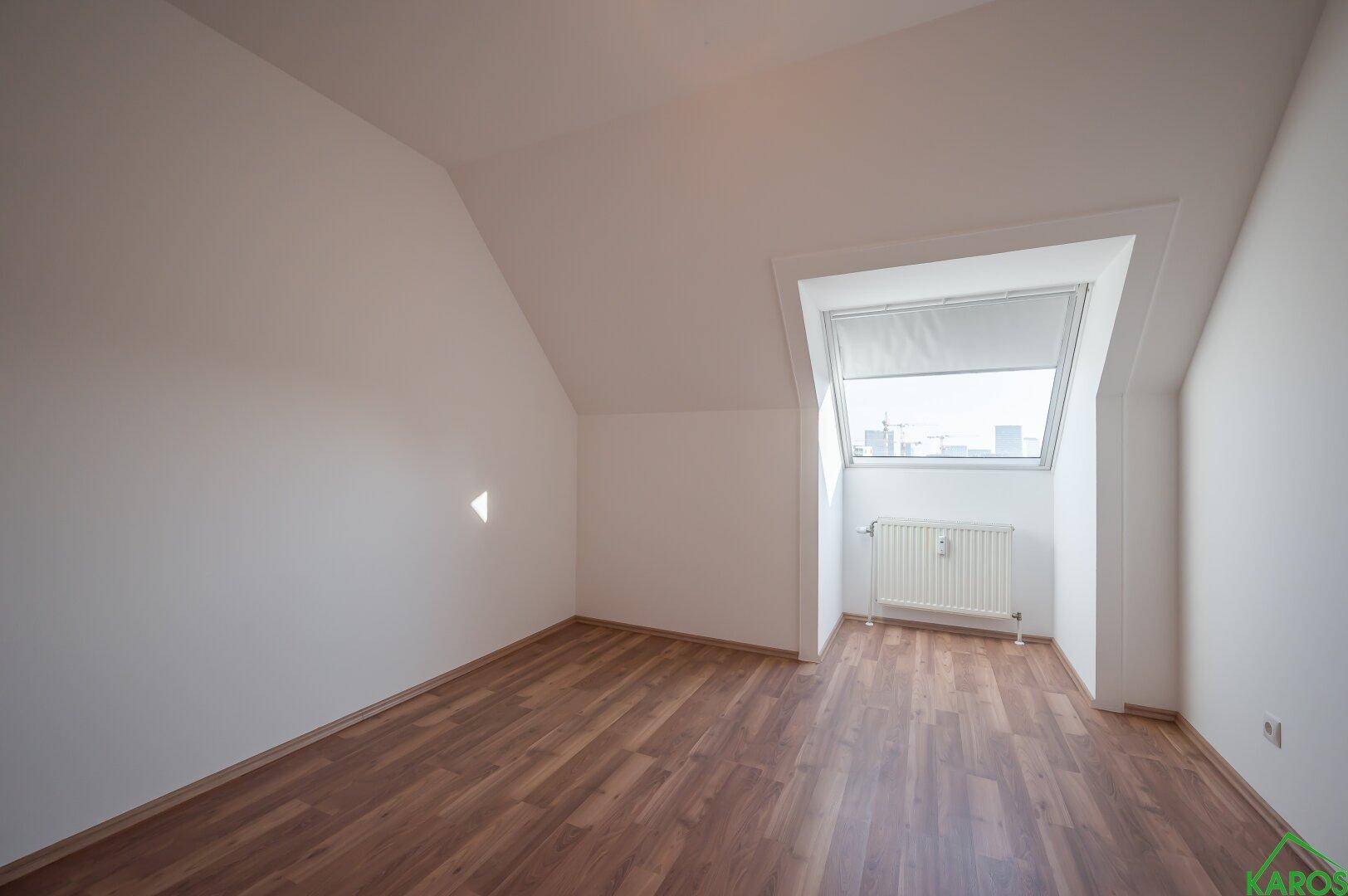 Helles Schlafzimmer im Dachgeschoss mit Laminatboden und einem Dachfenster.