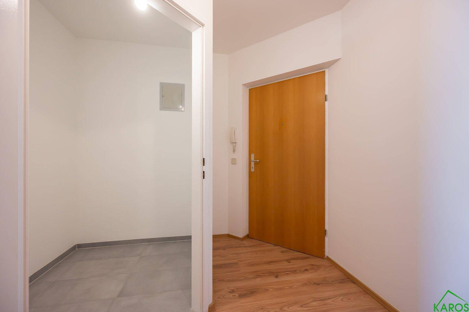 Eingangsbereich mit Holztür und angrenzendem gefliesten Bereich, der zu weiteren Räumen führt.