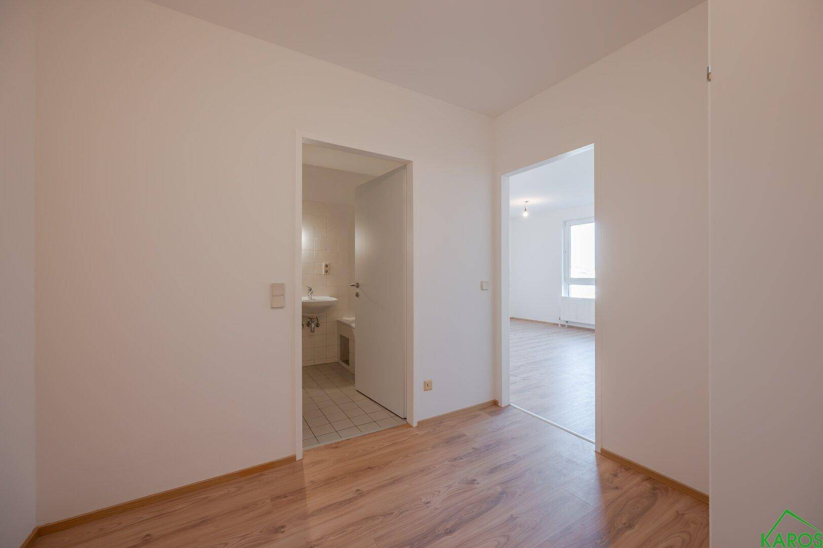 Flur mit Laminatboden, der den Zugang zu einem Badezimmer und einem weiteren Zimmer ermöglicht.
