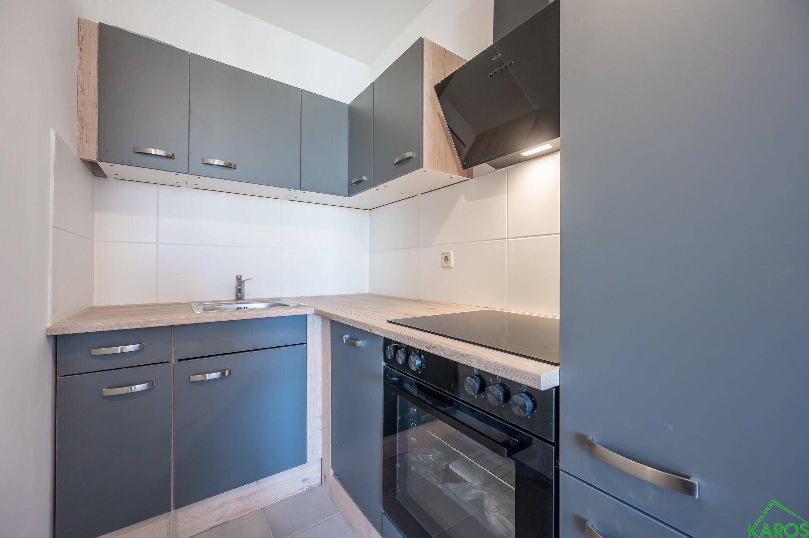 Moderne Einbauküche mit grauen Schränken, Holzoptik-Arbeitsplatte und Induktionskochfeld.