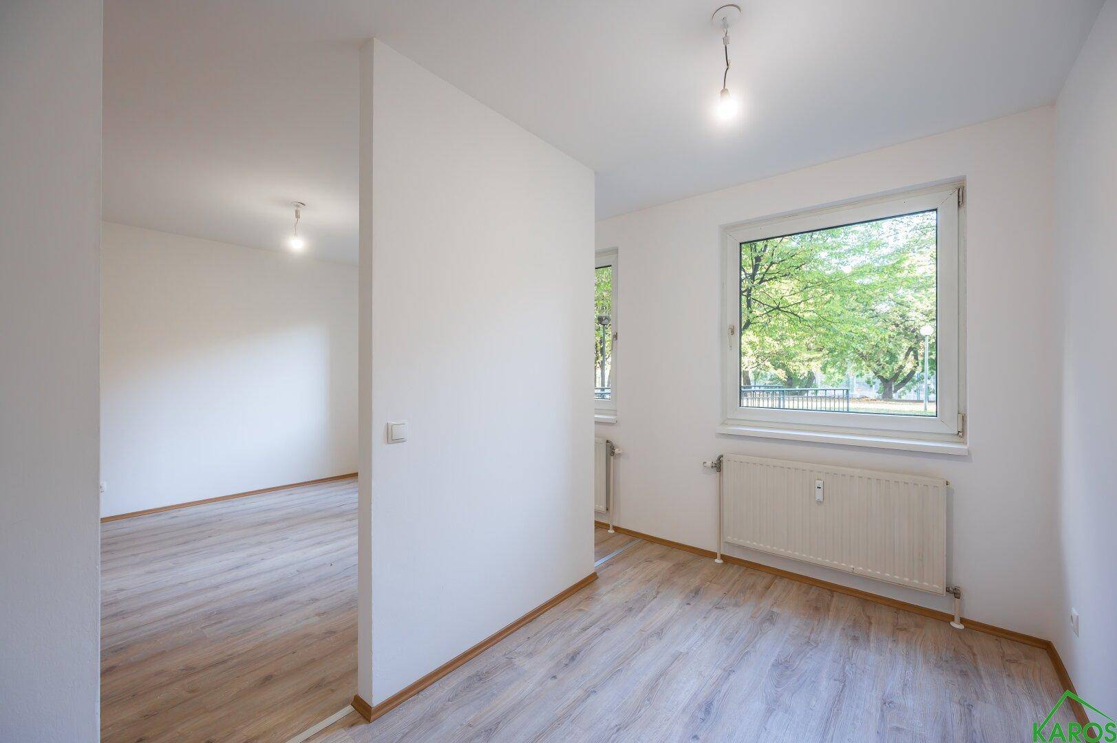 Lichtdurchfluteter Raum mit Laminatboden und einem großen Fenster, das einen Blick ins Grüne bietet.