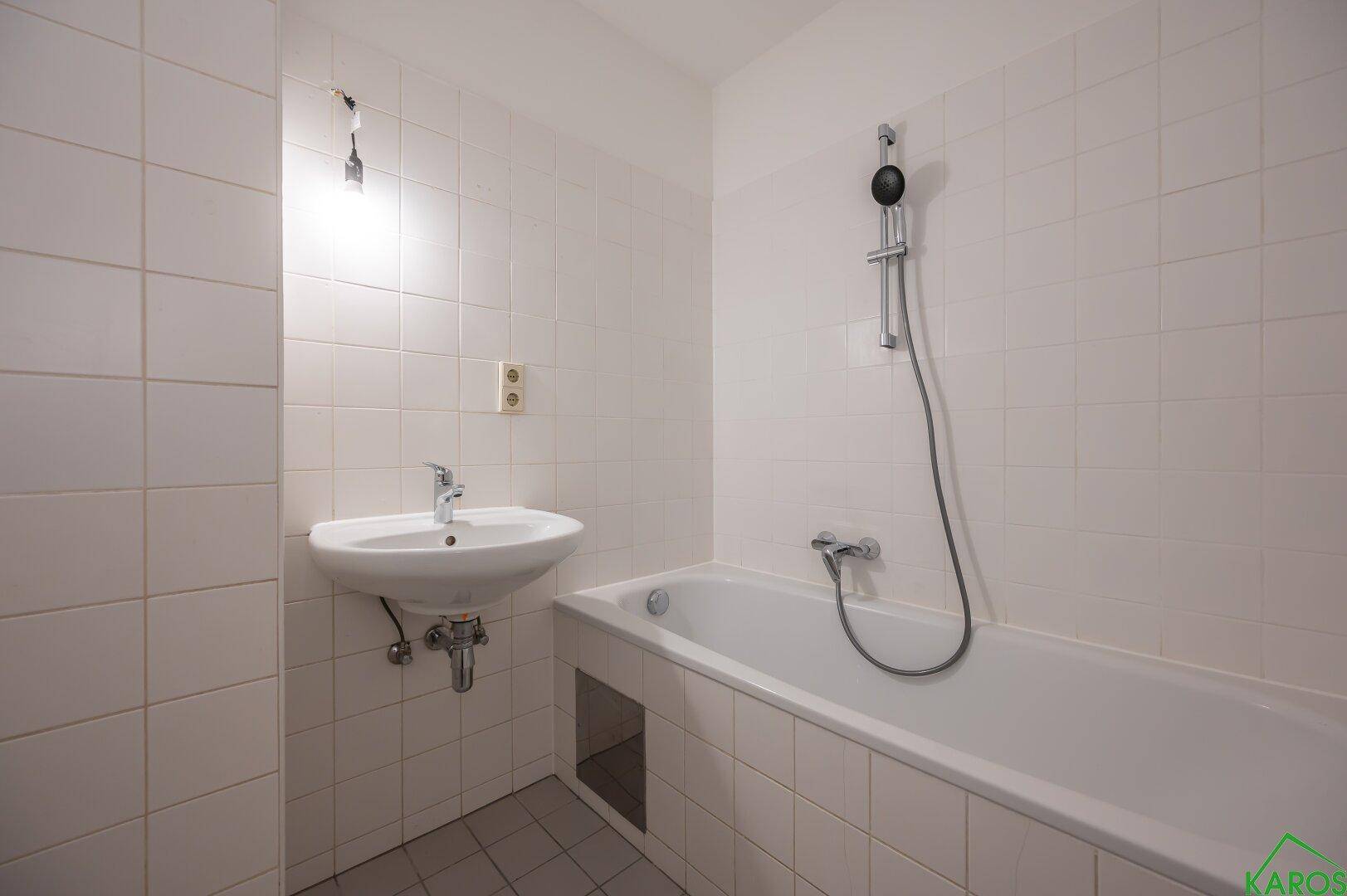 Funktionales Badezimmer mit Badewanne, Waschbecken und weißen Fliesen, in gutem Zustand.