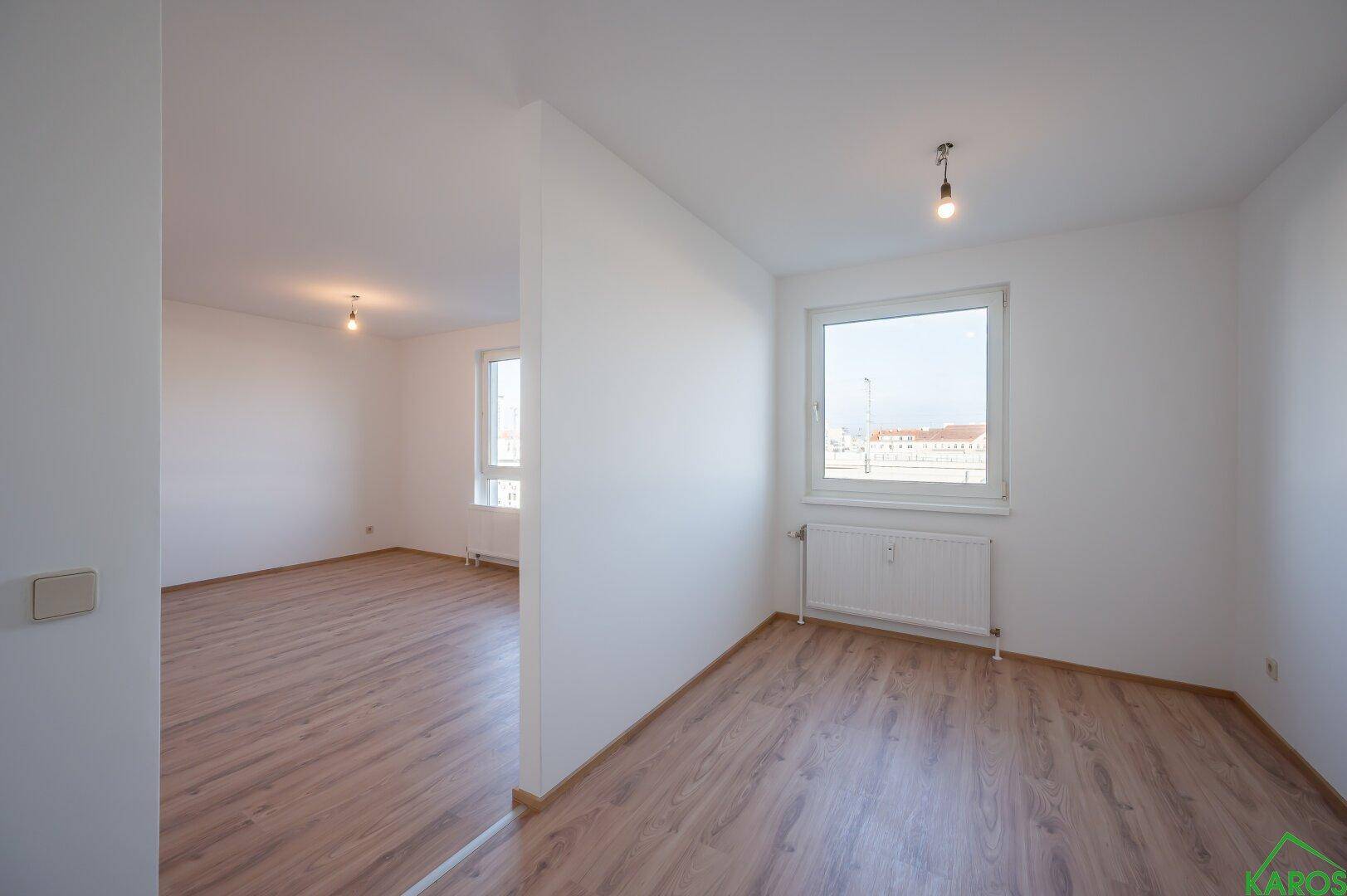 Geräumiger, heller Innenraum mit Laminatboden und großen Fenstern, ideal für Wohnzwecke.
