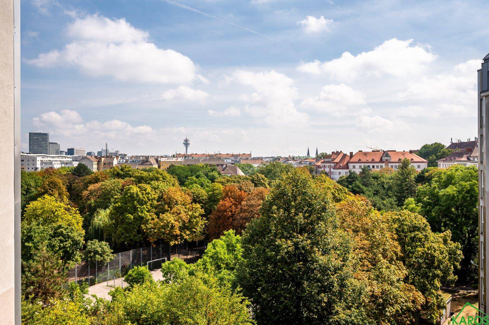 Weitläufiger Blick von einem Balkon über grüne Baumwipfel und die Stadtlandschaft am Horizont.