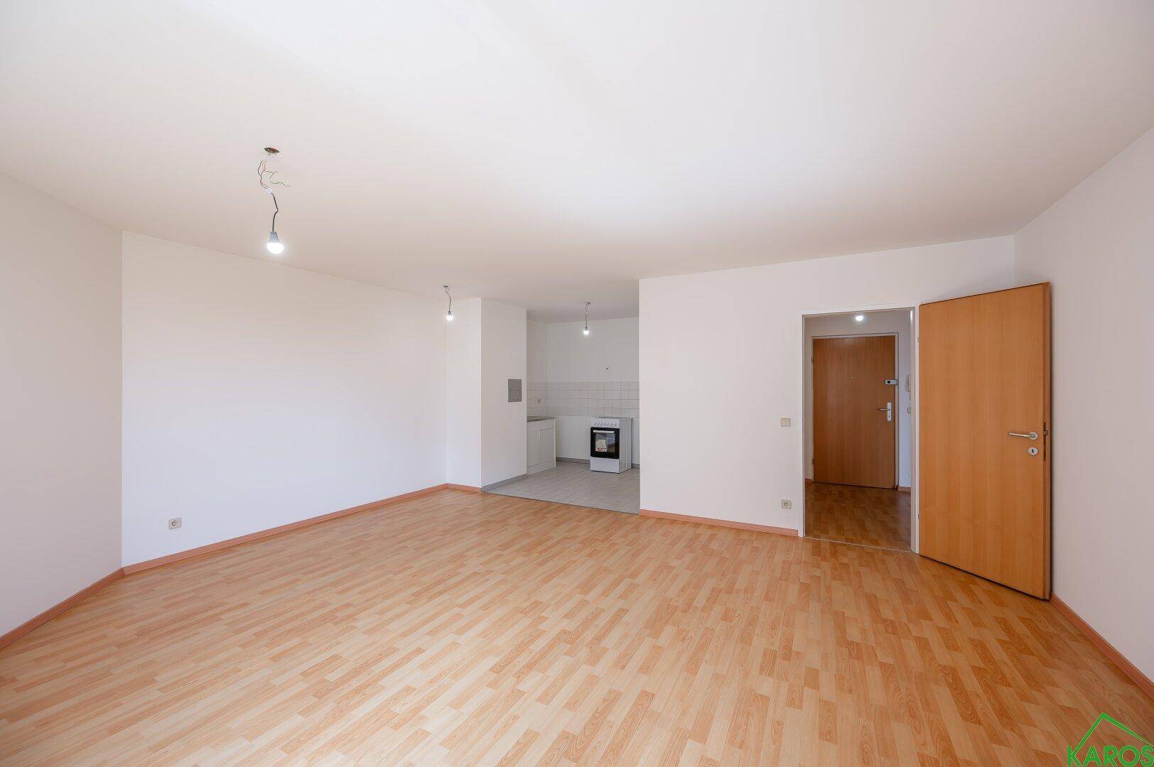 Offener Wohnbereich mit Laminatboden, der in eine kleine Küchenzeile übergeht, ideal für modernes Wohnen.