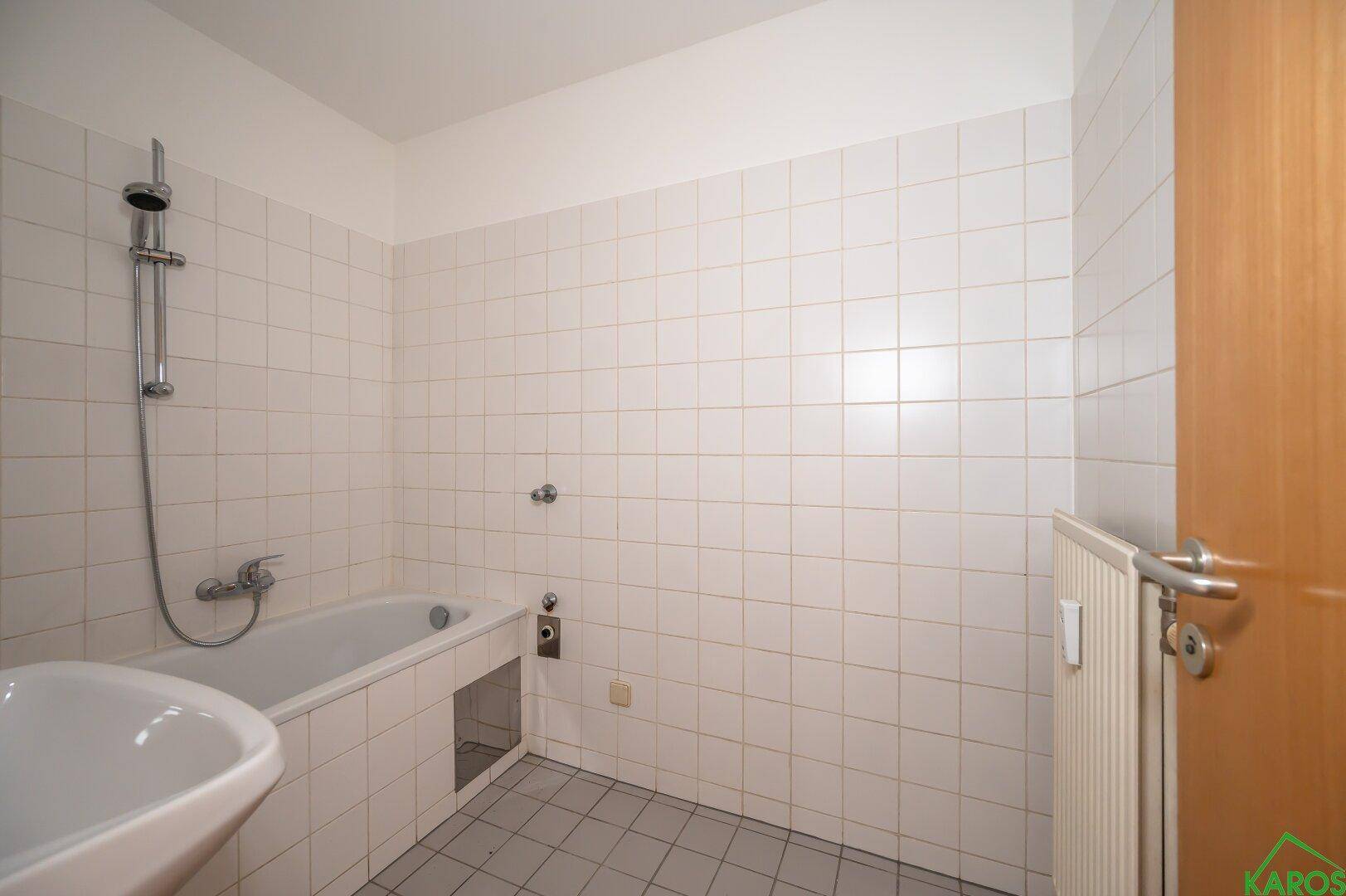 Badezimmer mit weiß gefliesten Wänden, einer Badewanne und einem Heizkörper, in gutem Zustand.