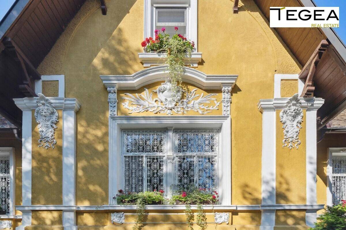 Detail der gelben Fassade mit kunstvollen Stuckverzierungen und Blumenkästen an den Fenstern.