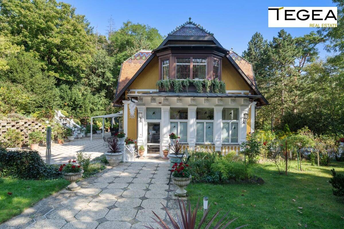 Frontansicht der historischen Villa mit Erker, gelber Fassade und gepflegtem Vorgarten mit Steinweg.