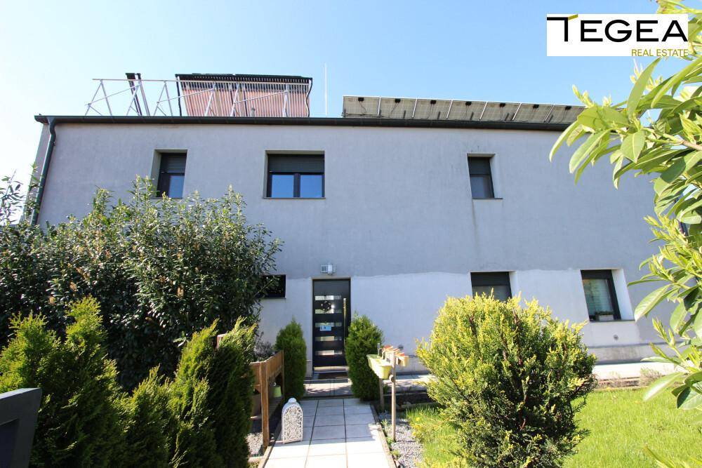 Moderne Hausfassade mit Eingangsbereich, umgeben von gepflegten Büschen und Solaranlagen auf dem Dach.
