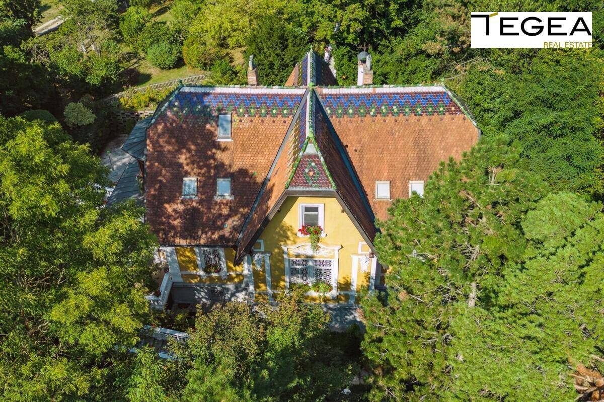 Nahaufnahme der historischen Villa mit gelber Fassade, verzierten Fenstern und farbenfrohem Dach.