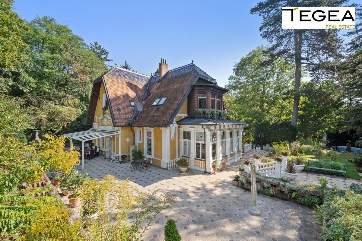 Historische Villa mit gelber Fassade, umgeben von einem gepflegten Garten und sonnigen Terrassenbereichen.
