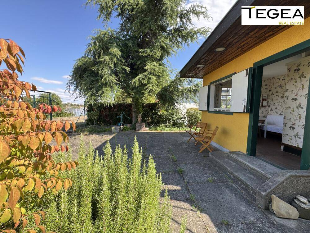 Gepflasterte Terrasse vor dem gelben Haus mit Sitzgelegenheiten und Blick ins Grüne.