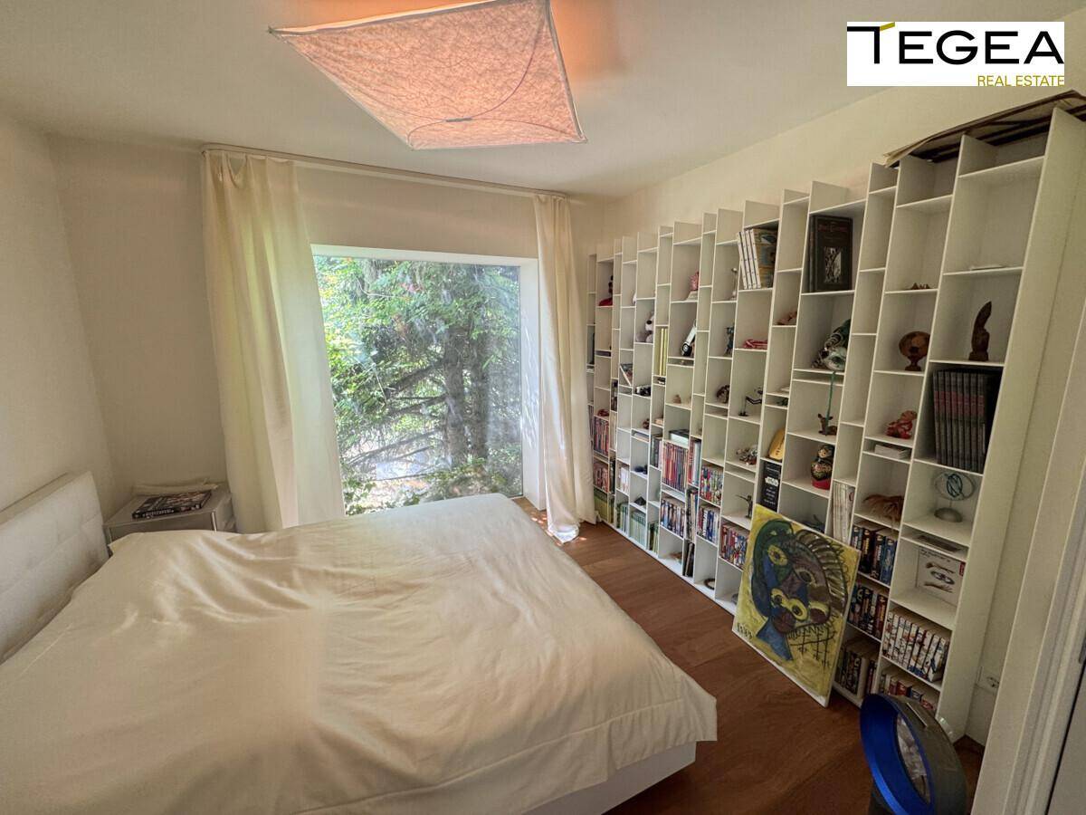 Helles Schlafzimmer mit großem Fenster, Holzboden und integriertem Bücherregal.