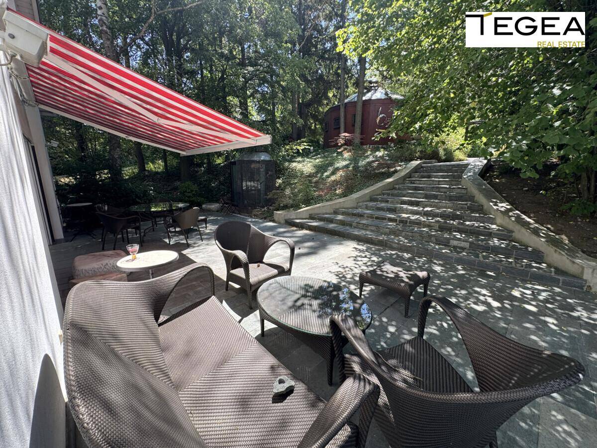 Große Terrasse mit Markise und Gartenmöbeln, führt über Steinstufen zu einem oberen Bereich.