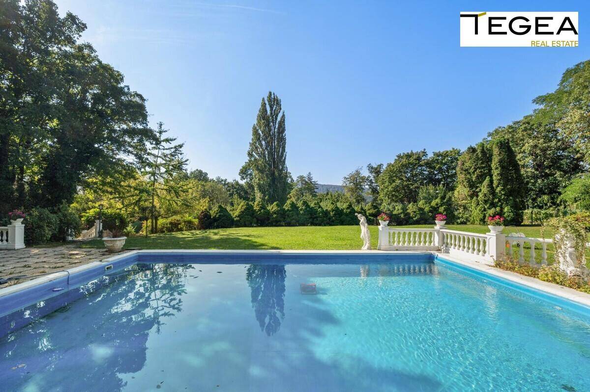 Außenpoolbereich mit weitläufiger Rasenfläche, umgeben von Bäumen und einer klassischen Balustrade.